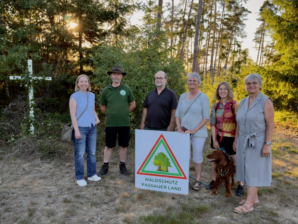 Sechs Personen stehen in einer Lichtung im Wald. Vor ihnen steht eine Tafel mit der Aufschrift "Waldschutz Passauer Land".
