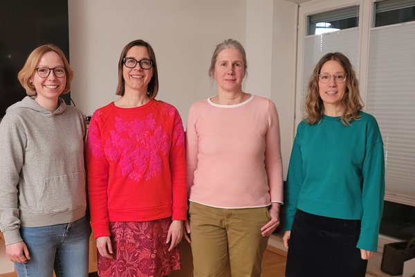 Vier Frauen posieren für ein Gruppenfoto. Sie stehen nebeneinander und lächeln in die Kamera.