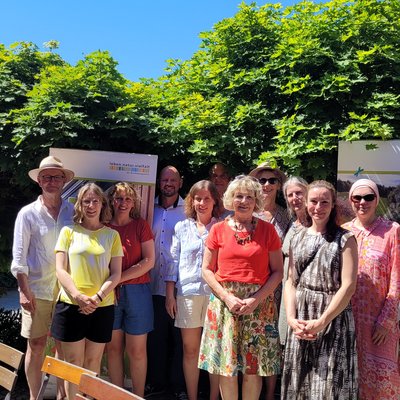 Mehrere Personen posieren als Gruppe für ein Foto. Sie sind in einem Biergarten. Die Sonne scheint. 