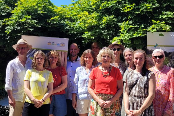Mehrere Personen posieren als Gruppe für ein Foto. Sie sind in einem Biergarten. Die Sonne scheint. 
