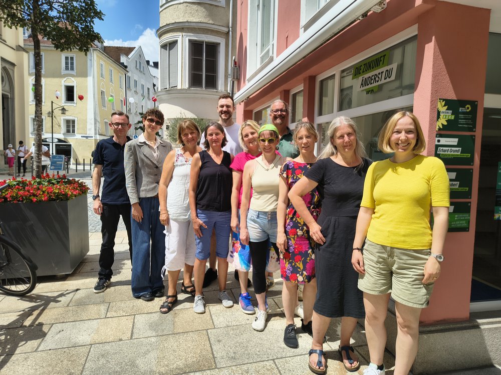 Elf Personen posieren für ein Gruppenfoto. Die Sonne scheint. Die Gruppe steht in einer Gasse der Stadt Passau.