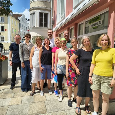 Elf Personen posieren für ein Gruppenfoto. Die Sonne scheint. Die Gruppe steht in einer Gasse der Stadt Passau.