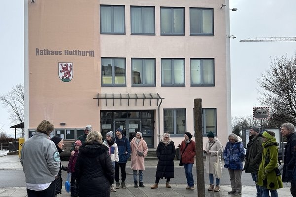 Etwa 15 Personen stehen vor dem Rathaus in Hutthurm. Sie hören einem Vortrag zu.