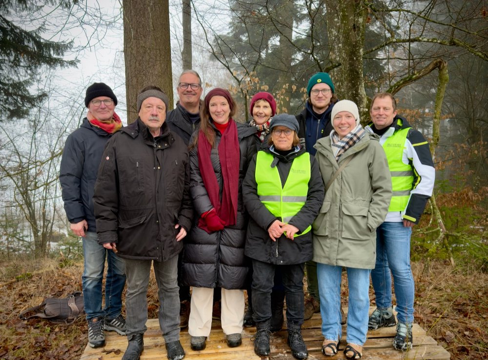 Eine Gruppe von neuen Personen posiert für ein Foto. Sie tragen Winterkleidung und stehen in einem Wald.