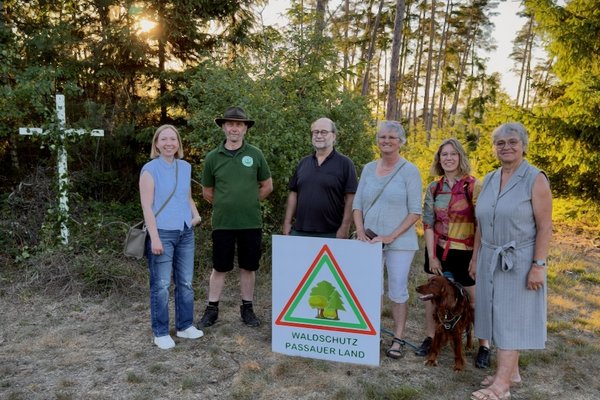 Sechs Personen stehen in einer Lichtung im Wald. Vor ihnen steht eine Tafel mit der Aufschrift "Waldschutz Passauer Land".