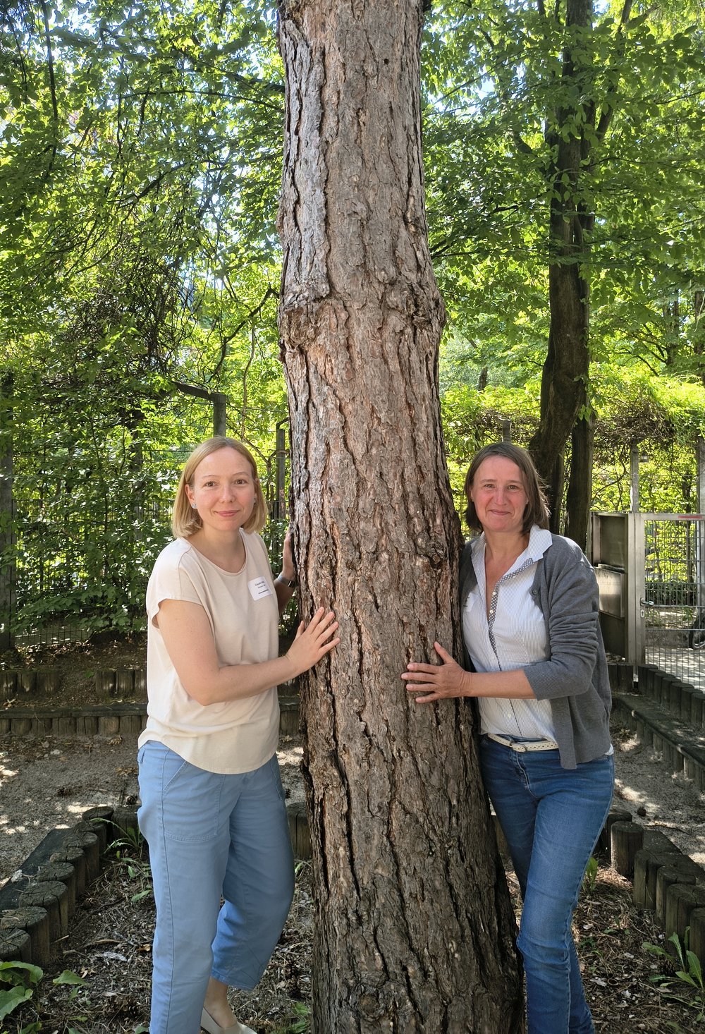 Zwei Frauen lehnen an einem Baum. Es ist Sommer.