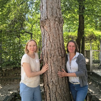 Zwei Frauen lehnen an einem Baum. Es ist Sommer.