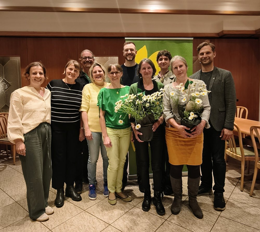 Zehn Personen posieren für ein Gruppenfoto. Zwei Personen halten Blumen in der Hand.