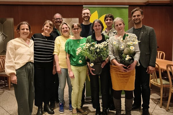 Zehn Personen posieren für ein Gruppenfoto. Zwei Personen halten Blumen in der Hand.